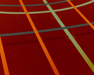 A sports court with intersecting lines in orange and blue, creating geometric patterns on a reddish-brown surface.